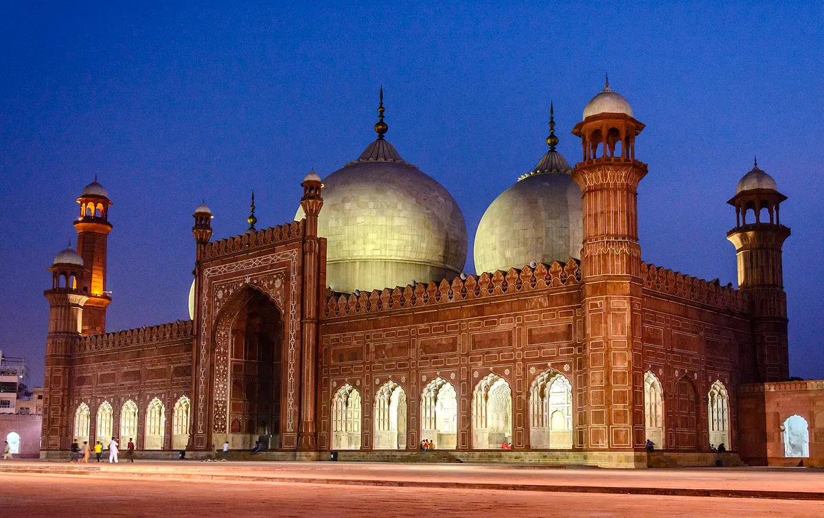 The domes and minarets of the Badshahi Mosque in Lahore, lit against a deep blue evening sky