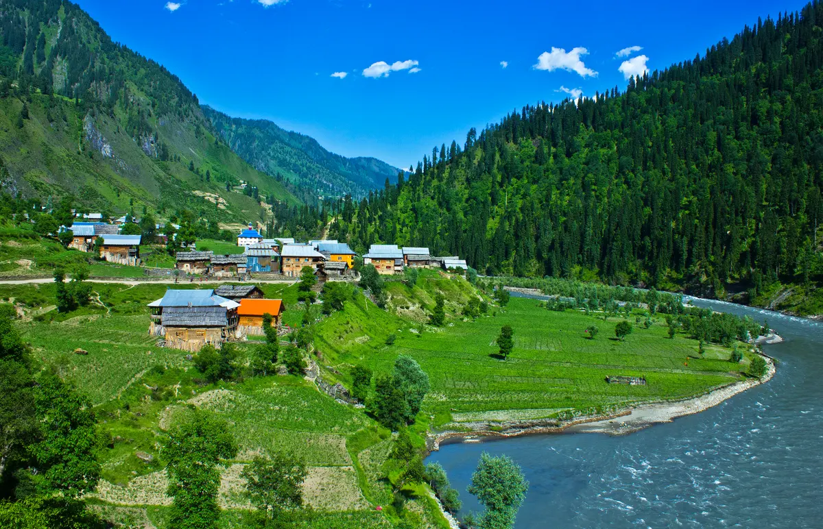A village of bright-roofed houses beside the Neelum River, with pine forest climbing the valley walls