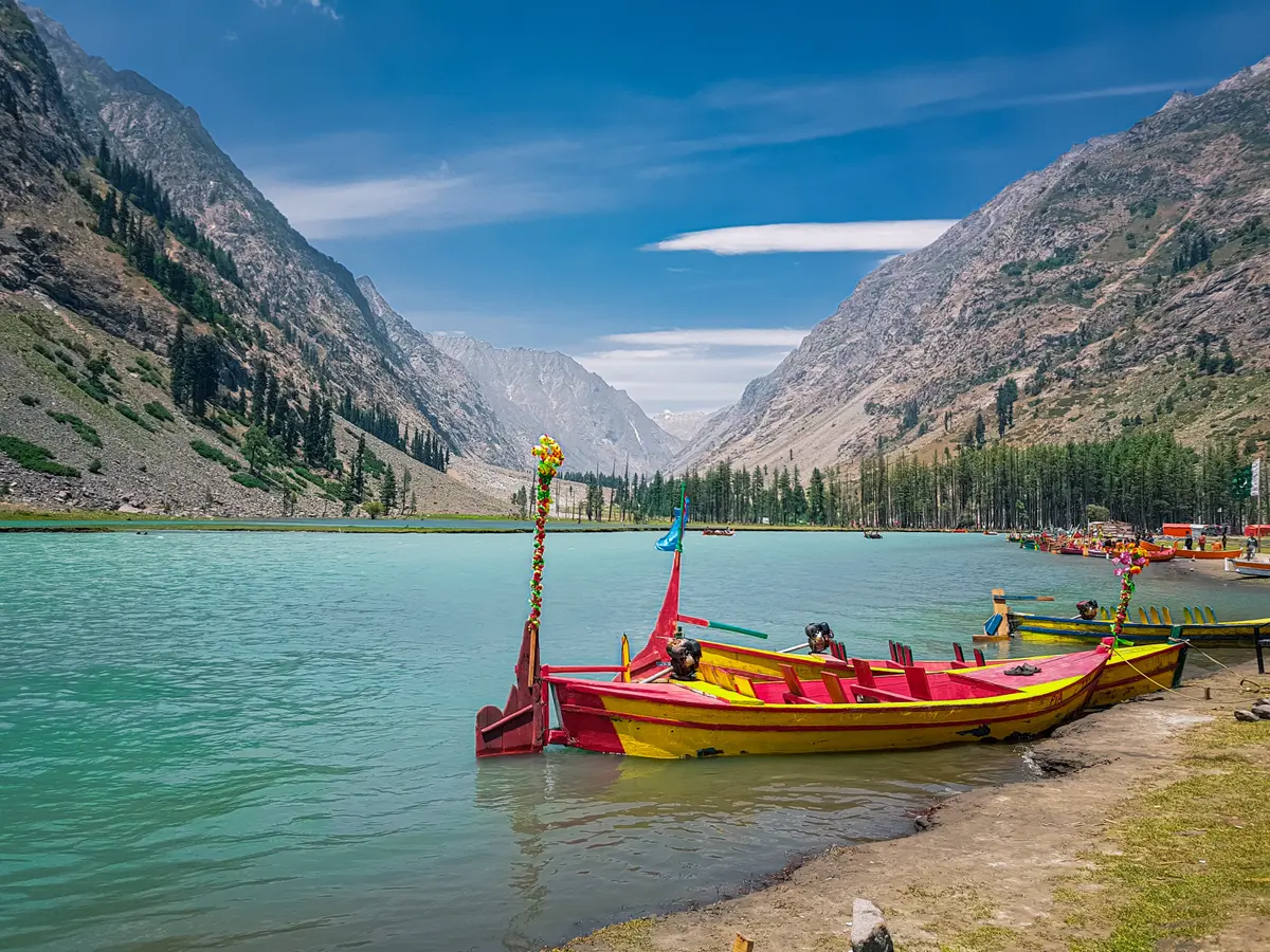 Painted wooden boats on the blue-green water of Mahodand Lake, ringed by pine forest in upper Swat